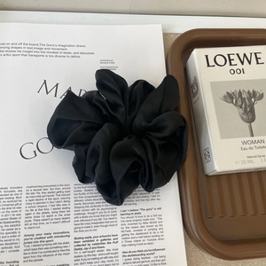 Detail of a large black satin silk scrunchie with soft folds on a fashion magazine