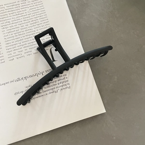 Close-up of a matte black metal hair claw clip resting on a white book for styling