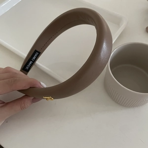 Gros plan sur le serre-tête en similicuir marron café avec logo doré et étiquette fait main