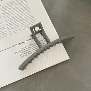 Close-up of matte sage green large metal shark hair claw clip on a vintage book