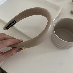 Détail d'un serre-tête rembourré en similicuir beige avec lettre P dorée et étiquette