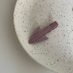 Detail view of a matte lavender kite-shaped hair clip on a cream speckled ceramic plate