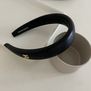 Gros plan du bandeau en cuir noir avec lettre R en métal doré et étiquette fait main