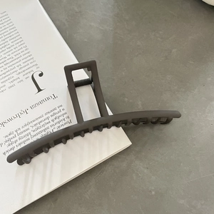 Matte dark grey oversized rectangular shark hair claw clip on a minimalist book background