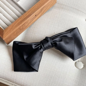 Detail of elegant black satin bow hair clip featuring smooth silk texture and premium finish
