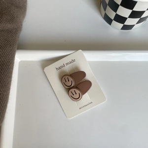 Detail of two cute brown bear-toned smiley face hair clips on a handmade card display