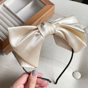 Detail of elegant cream satin oversized bow headband with smooth silk texture