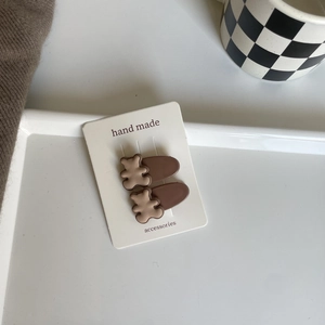 Close-up of two cute brown bear hair clips on a white paper card with handmade logo
