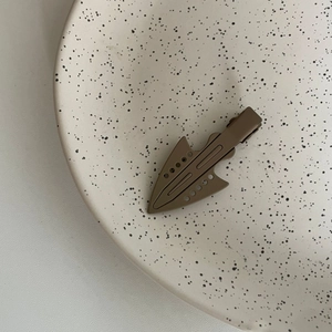 Close-up of matte brown arrow-shaped hair clip on a textured black ceramic tray