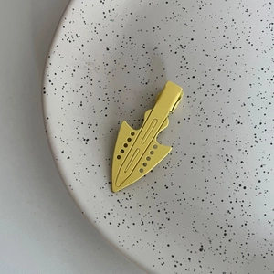 Close-up of matte yellow arrow-shaped metal hair clip on a ceramic tray detail