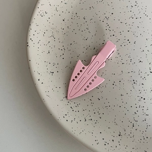 Pink matte metal hair clip with geometric hollow design on a beige ceramic plate