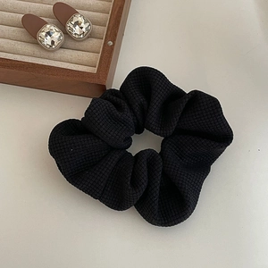 Vue détaillée du chouchou noir en maille gaufrée avec texture épaisse sur plateau bois