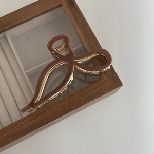 Close-up of a brown acetate bow hair claw clip with golden metal details on a jewelry box