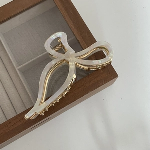 Detail view of a white bow hair claw clip with golden teeth on a wooden jewelry box