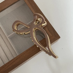 Elegant bow-shaped hair claw clip in mocha resin and gold frame on a wooden box