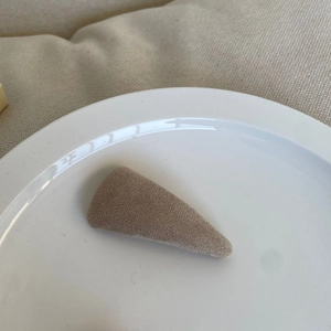 Detail of a beige flocked triangle hair clip placed on a minimalist ceramic plate