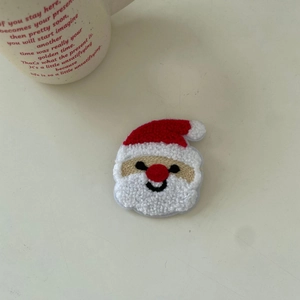 Detail of Christmas Santa plush embroidered hair clip on a minimalist desk setup