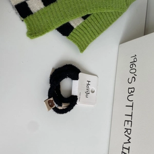 Detail shot of black plush hair scrunchie featuring a cute brown bear patch and white tag