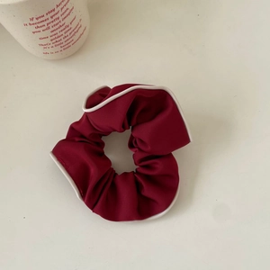Detail of burgundy hair scrunchie with white piping edge on a minimalist desk setup