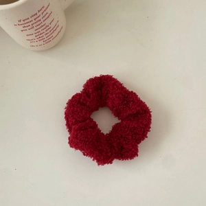 Close-up of a plush red velvet scrunchie on a white desk with a coffee mug