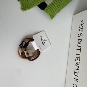 Close-up of four brown and beige plush elastic hair ties with decorative fabric labels