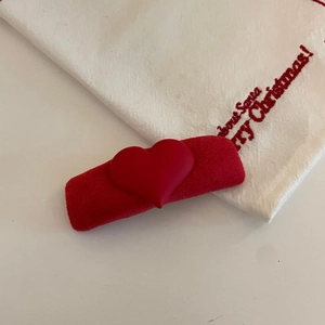 Detailaufnahme einer roten Herz-Haarklammer mit mattem Finish auf festlichem weißem Stoff