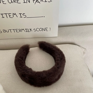 Detailed view of wide faux rabbit fur headband in dark brown on a beige fabric background