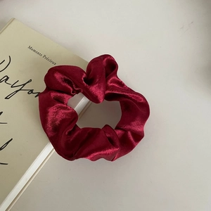 Detail of a burgundy satin scrunchie resting on a vintage book with elegant folds