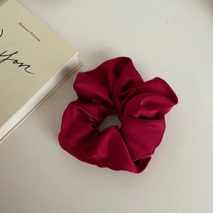 Close-up of a premium deep red satin scrunchie with silk texture on beige background