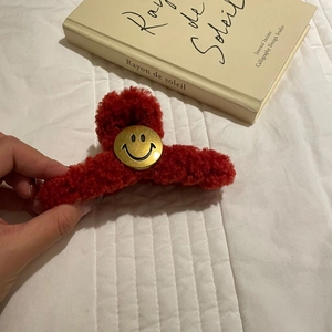 Close-up of a festive red plush claw clip with a golden smiley face accent for hair styling