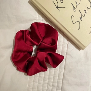 Close-up of a festive red satin scrunchie on a white quilted background with a book