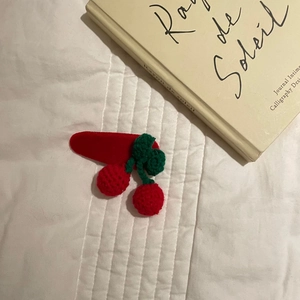 Detail of handmade crochet cherry hair clip with green leaves on white quilted fabric