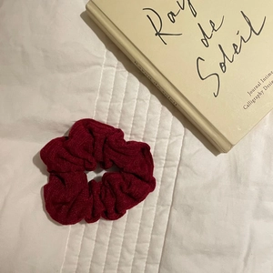 Detailed view of a dark red pleated scrunchie with soft velvet texture on a white surface