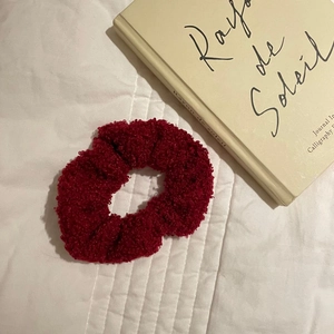 Close-up of fluffy red lamb wool hair scrunchie on a cozy white bed with a book
