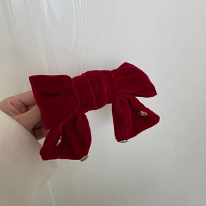 Elegant red velvet bow hair clip with gold pendants shown in a hand-held display