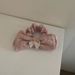 Coletero rosa con estampado floral, lazo grande y detalle de perla dorada elegante