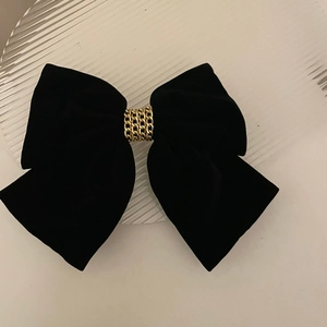 Detail of black velvet bow hair clip featuring elegant gold chain accents on a tray
