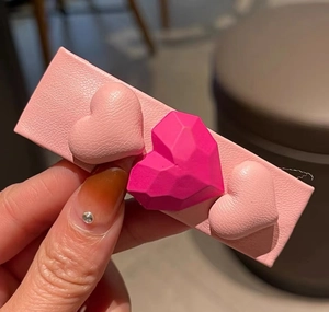 Détail macro d'une pince à cheveux en cuir rose avec trois cœurs 3D et facettes