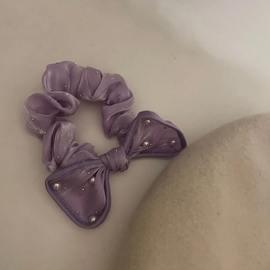Détail d'un chouchou en satin violet avec nœud et perles blanches sur tissu lisse