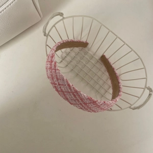 Détail d'un serre-tête en tweed rose et blanc placé dans un panier de rangement en métal