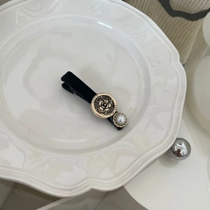 Detailed shot of camellia motif and faux pearl on black velvet duckbill hair clip