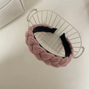 Détail d'un bandeau tricoté rose poudré avec motif à rayures dans un panier blanc