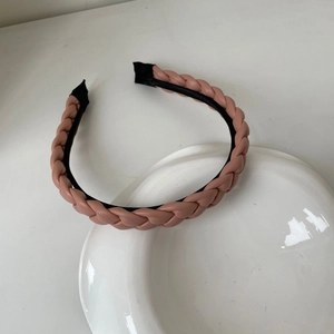 Gros plan du serre-tête tressé en cuir rose avec bordure noire sur une assiette blanche