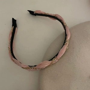 Elegante cerchietto in tessuto rosa con catena dorata e perle su sfondo minimalista