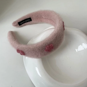Gros plan d'un bandeau en peluche rose avec fleurs et étiquette faite main sur plateau