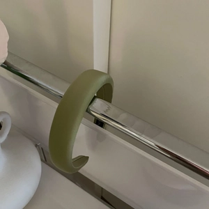 Detailed view of thick matcha green satin headband hanging on a sleek metal stand
