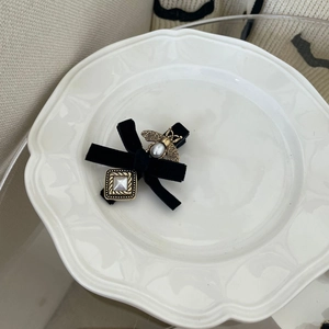 Detail view of a black velvet bow hair clip with gold bee and pearl accents on white ceramic