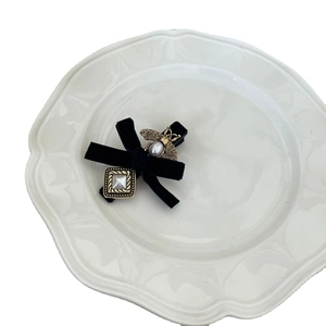 French velvet bow hair clip with golden bee and pearl detail on a white ceramic plate