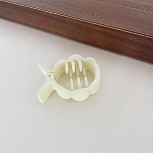 Dettaglio macro della pinza per capelli in acrilico crema con bordi a petalo e denti interni