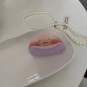 Elegant purple acetate hair claw clip with a semi-circle design on a white ceramic plate